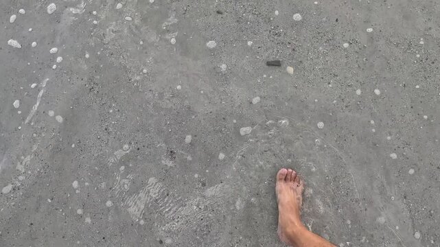 An aerial video showing feet walking on the sand towards the sea.