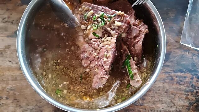 Hot oxtail soup served in a small pot on a wooden table.