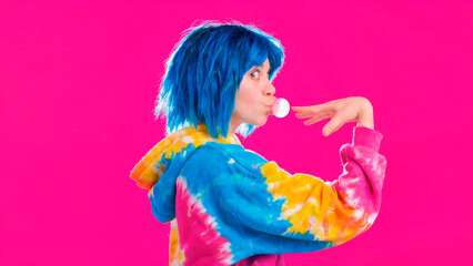 Fototapeta premium Profile of a young person with bright blue hair blowing a bubblegum bubble against a vibrant pink background