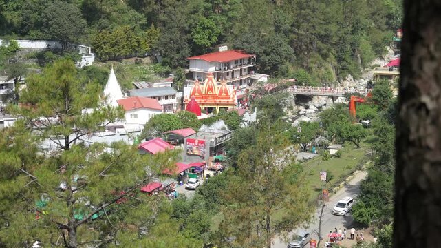 Scenic view of Kainchi Dham temple, a famous spiritual site associated with Neem Karoli Baba, located near Bhowali in Nainital, Uttarakhand, India. Surrounded by lush green hills, buildings, and a bri