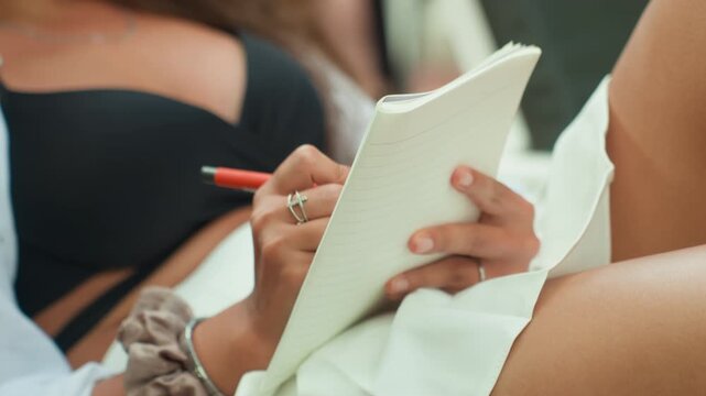 Woman on island lounger writing notes, travel blogger planning sunrise itinerary with pen and textured notebook, black bikini top, rings and scrunchie, sunlit resort mood, closeup of hands and pages