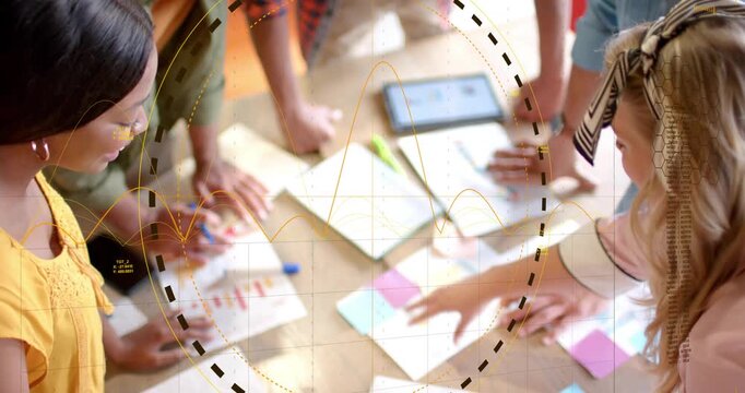 Diverse coworkers collaborating around wood table in office with tablet arranging sticky notes
