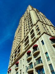 Fototapeta premium Tall building reaches for the blue sky in a city with clear weather and bright sunlight, showcasing its architecture and design from a low angle view