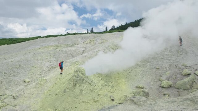 Person approaches the actively smoking fumarole on the wild volcanic area of the volcano of Mendeleev on Kunashir Island in Russia