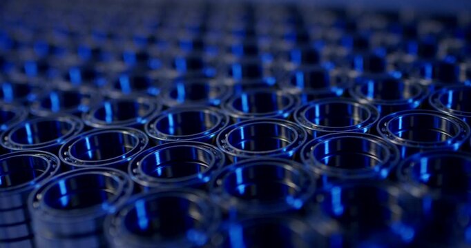 Large group of steel ball bearings arranged in rows with blue light reflection and shallow depth of field