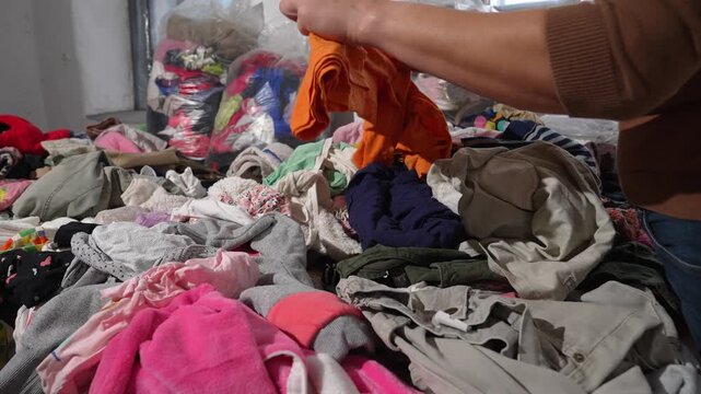 Woman sorting through pile of old clothes textile waste recycling concept