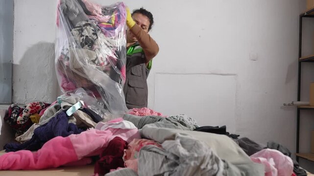 Female worker in uniform sorting large pile of used clothes in recycling facility. Donate your old clothes, shoes. Textile Recycling