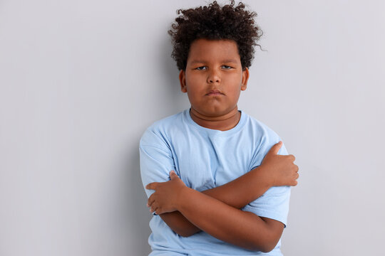 Portrait of resentful little boy with crossed arms on light grey background. Space for text