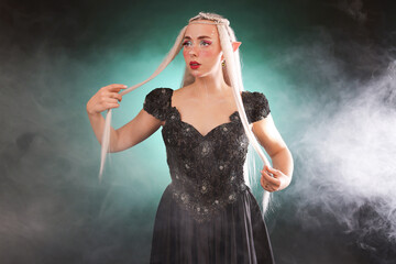 Naklejka premium Beautiful girl dressed as elf on dark background with smoke