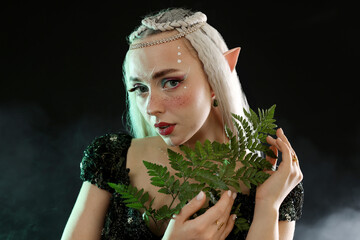 Naklejka premium Beautiful elf girl with floral decor on black background with smoke