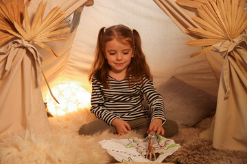 Little girl with drawing of map and toy giraffe near wigwam at home © New Africa