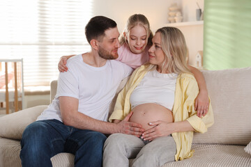 Obraz premium Pregnant woman with her daughter and husband on sofa at home