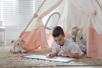 Little boy drawing in sketchbook near toy wigwam at home © New Africa