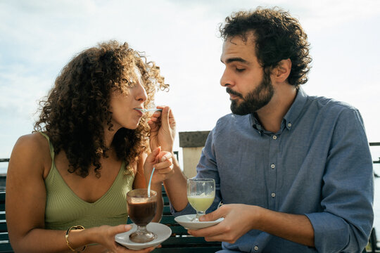 Couple sharing dessert and smiling together during sunny summer day