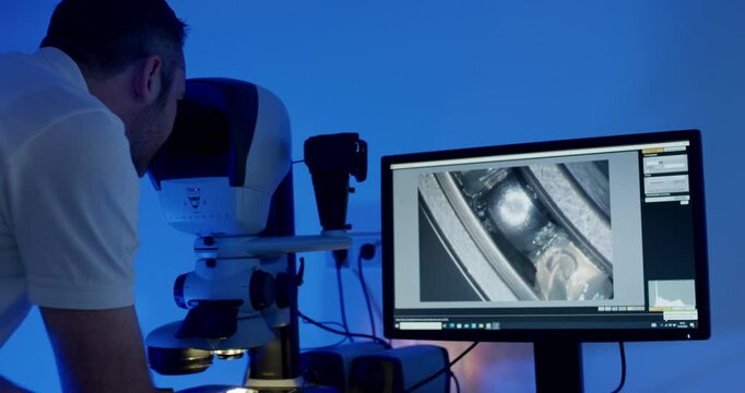 Engineer examining metal part through digital microscope with monitor display in laboratory
