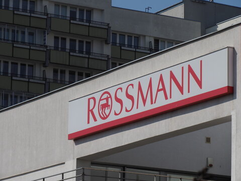 Signboard of Rossmann drugstore on a white building wall under a clear sky