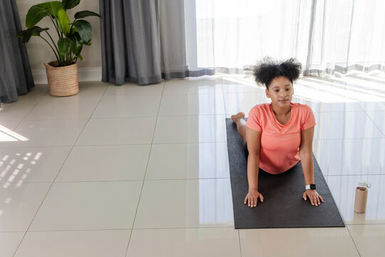 African American woman wearing coral top doing backbend on black yoga mat at home, copy space