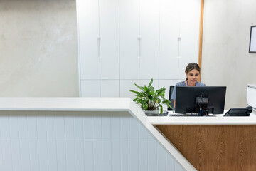 African woman receptionist in grey scrubs using monitor behind wood counter with plant, copy space © wavebreak3