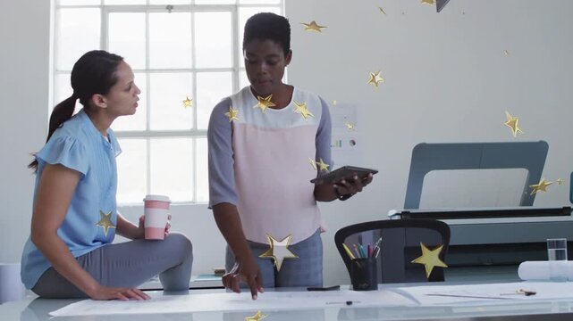 Female coworkers reviewing plans at desk, standing colleague pointing with tablet to decide design