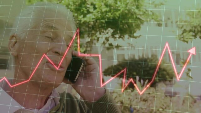 Senior male taking call on phone laughing listening under trees while red graph over grid rising