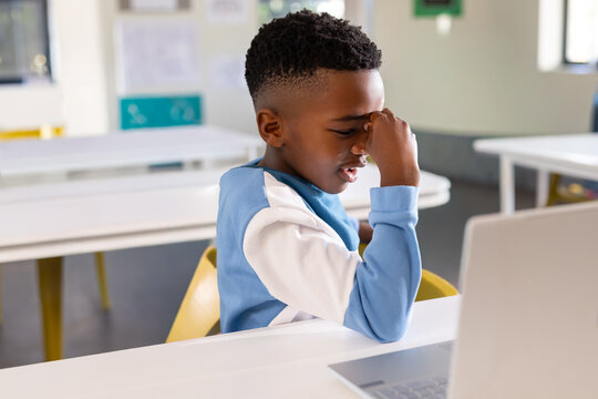 African American youth sitting at class desk on yellow chair using laptop in blue-top, copy space