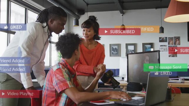 Seated creator tapping laptop and activating social notifications, team reacting and editing camera