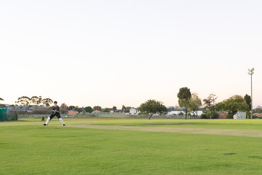Teenage male cricketer standing ready on cricket pitch wearing keeper gloves and pads, copy space