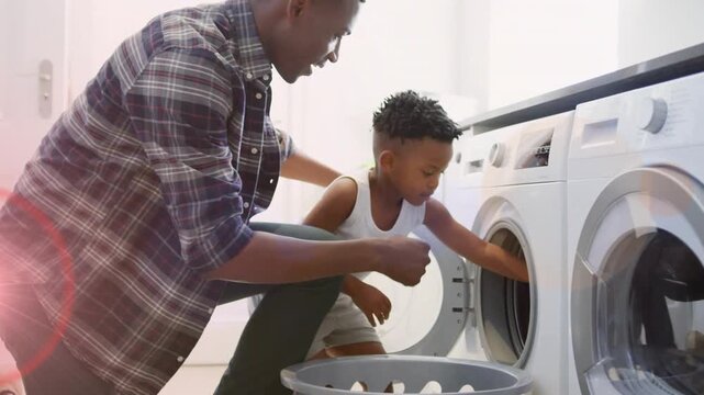 Father guiding son after child opening washer door, both loading garments for household laundry