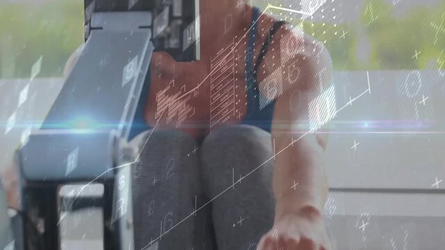 Woman gripping handle and rowing on ergometer beside monitor, animated charts tracking fitness
