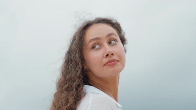 Woman with flowing hair views serene coast. Back view of lady watching peaceful island scene by sea. Profile of woman with windswept hair gazing across calm ocean and rugged cliffs