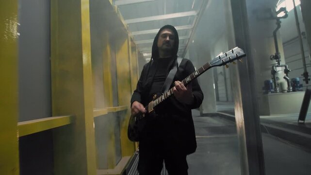 Close-up of an emotional rock singer in a black shirt inside a factory, he is performing intensely with dramatic hand gestures and expression