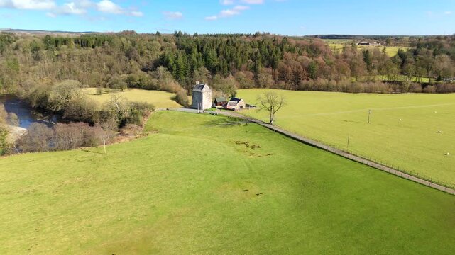 The River Esk winds through green fields and dense trees in the Scottish Borders. This scene shows a clear view of the landscape near Langholm on the A7. Hills rise in the background