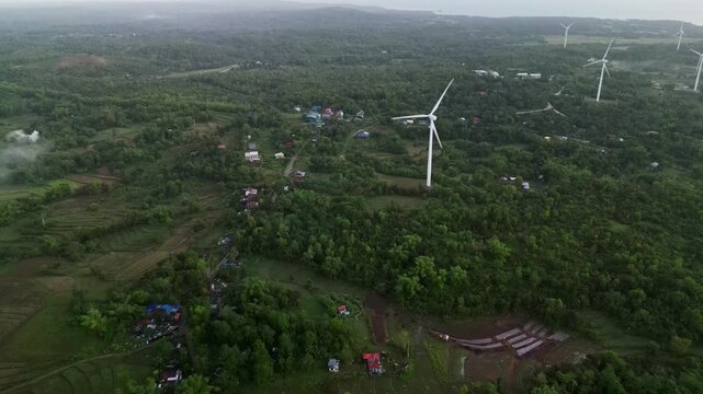 Aerial overview of wind turbines amid lush greenery at tropical barangay village and farmland - Guimaras island, Visayas, Philippines