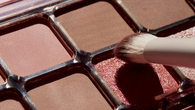 Macro close-up of makeup brush picking up nude eyeshadow powder, soft texture and natural tones highlighted. Ideal for beauty tutorials, cosmetic advertising and makeup education