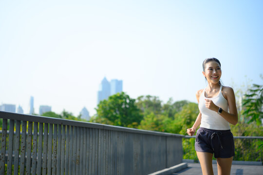 young fitness woman runner running on skywalk in park with urban city
