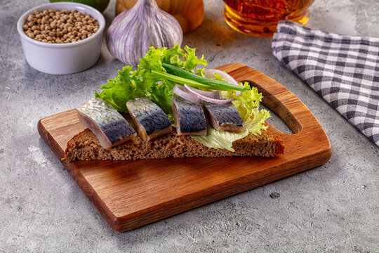 Salted herring appetizer on dark rye bread with lettuce and onions on a wooden board