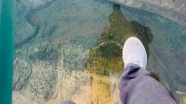 Person Walking on a Transparent Glass Bridge Above a Deep Canyon POV