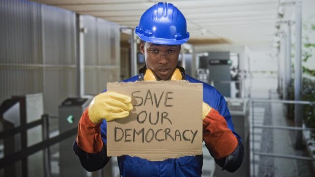 Man holding cardboard sign with gloved hands reading save our democracy in building entrance; civic protest concern.