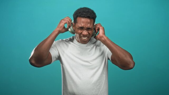 Man adjusting overear headphones with hands, eyes closed and smiling, wearing tshirt against teal studio set; pure joy.