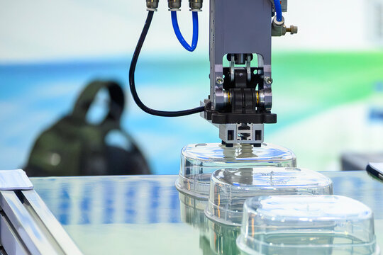 Industrial robotic arm placing plastic food containers onto a conveyor belt from an injection molding machine.
