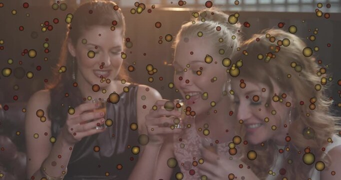 Animation of yellow spots bouncing over three female friends toasting and drinking shots at a bar