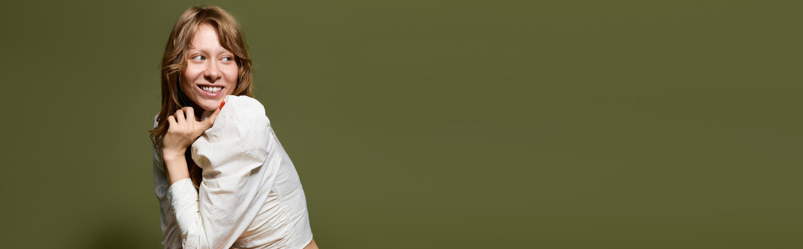 Stylish young woman poses joyfully against a serene olive green backdrop