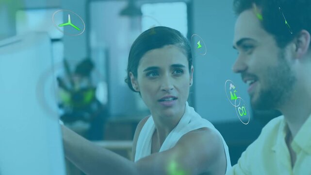 Woman reaching monitor during energy meeting, generating floating green icons while man smiling