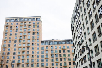 Fototapeta premium Modern high-rise apartment buildings stand tall. Light-colored facades and uniform windows dominate the scene. The sky is overcast, adding softness to the urban landscape