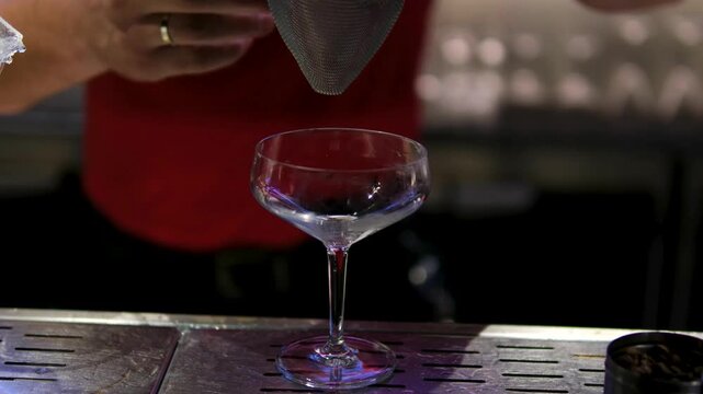 Bartender pouring orange brown cocktail through strainer chilled glass bar Europe nightlife drink preparation