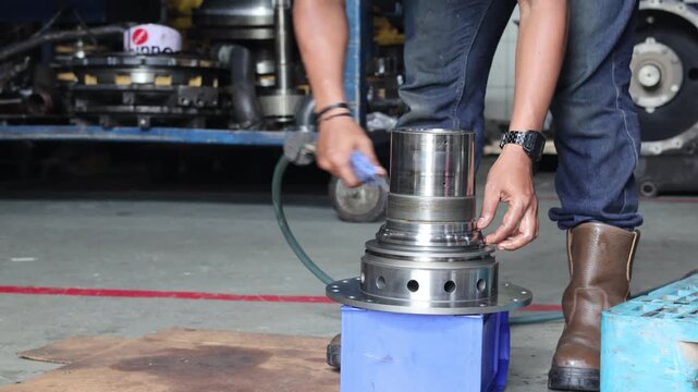 A mechanic uses a pneumatic air gun to blow dust off a metal transmission stator hub shaft in a workshop, ensuring a clean component surface during an industrial machinery maintenance process.
