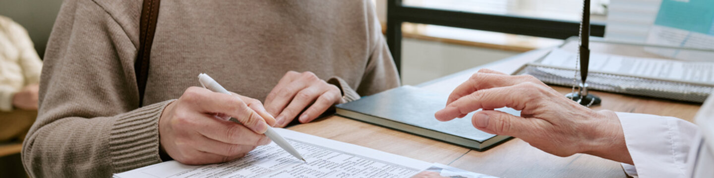 Patient signing medical form while doctor pointing at paperwork during clinic visit, illustrating patient intake and consent process for healthcare marketing and insurance
