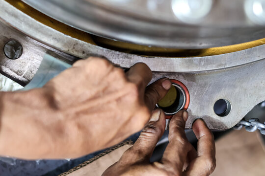 Close up of a mechanic installing orange rubber O-ring seals into a heavy metal industrial engine component in a workshop during a professional machinery maintenance.