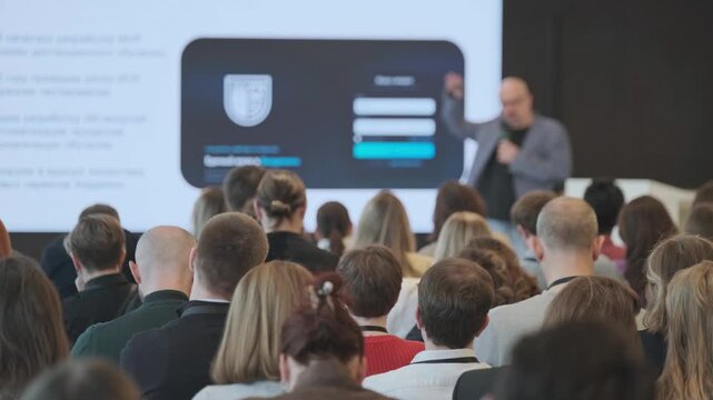 Business conference audience seated, listening to presenter and slideshow about technology and product development. Professional networking, learning, collaboration.