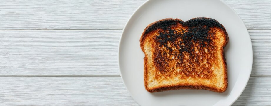 rustic breakfast fail Single slice of burnt bread toast on white plate on rustic wooden kitchen table with natural light and minimal composition creating simple everyday food moment